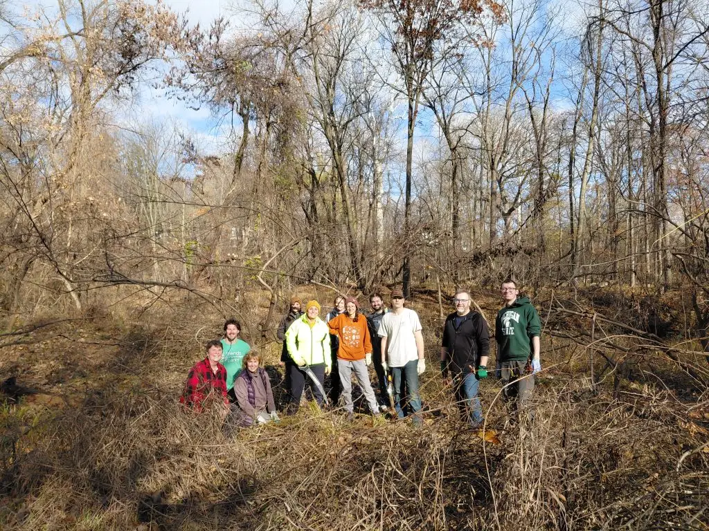 group of people standing in the woods in fall holding hand tools like loppers
